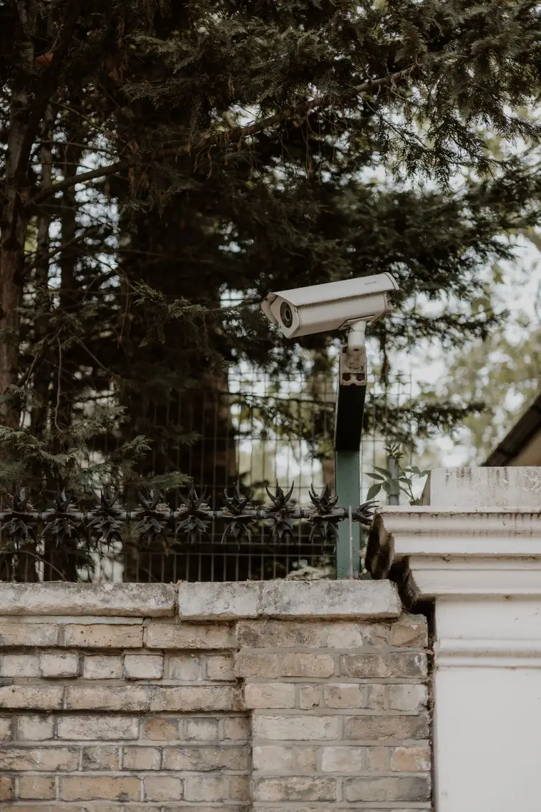 Outdoor security camera on a post above a garden fence