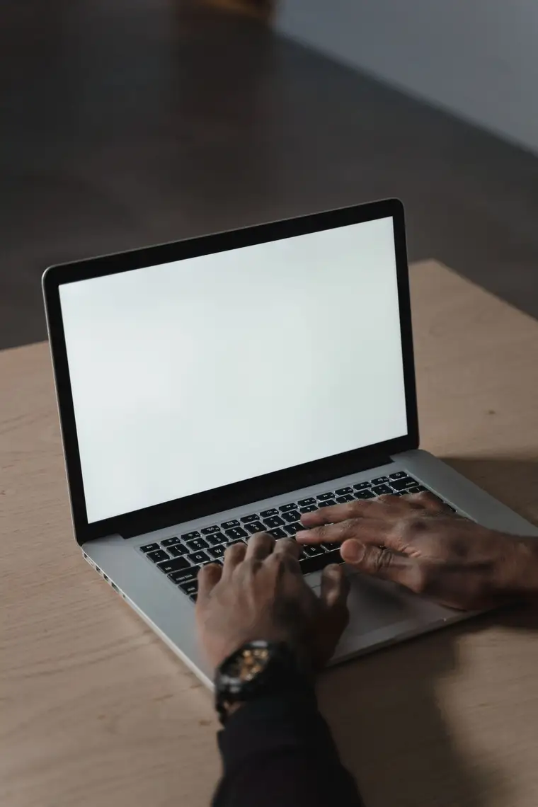 Hands typing on a laptop with a blank white screen